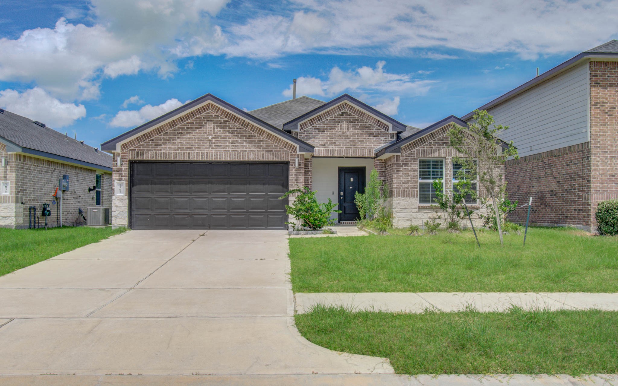 7903 Wrangler Shack Lane Rosharon, TX 77583 - Photo 1 of 29 Discover modern living in this charming single-story brick home, featuring a two-car garage, a pristine front yard with a small garden, and a sleek concrete driveway, all set beneath a brilliant blue sky.