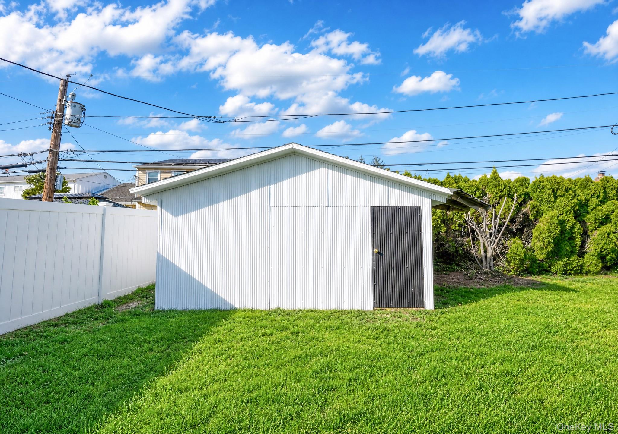 61 Cheshire Road Bethpage, NY 11714 - Photo 25 of 25 White corrugated metal shed with a dark panel door, set within a vibrant green lawn