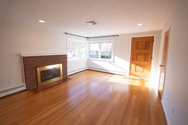 a view of an empty room with wooden floor fireplace and a window