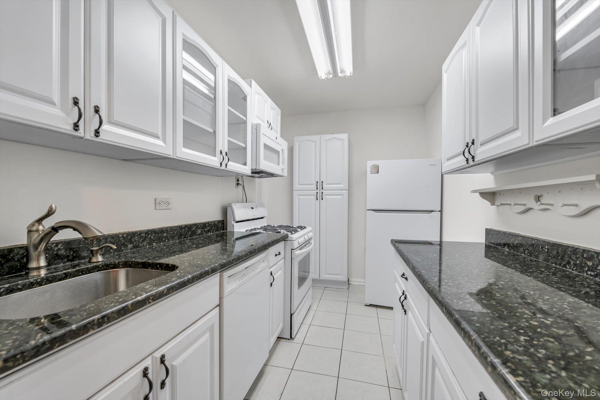 123-35 82nd Road, Unit 4H Queens, NY 11415 - Photo 5 of 15 Kitchen with glass insert cabinets, white appliances, white cabinets, and dark stone countertops