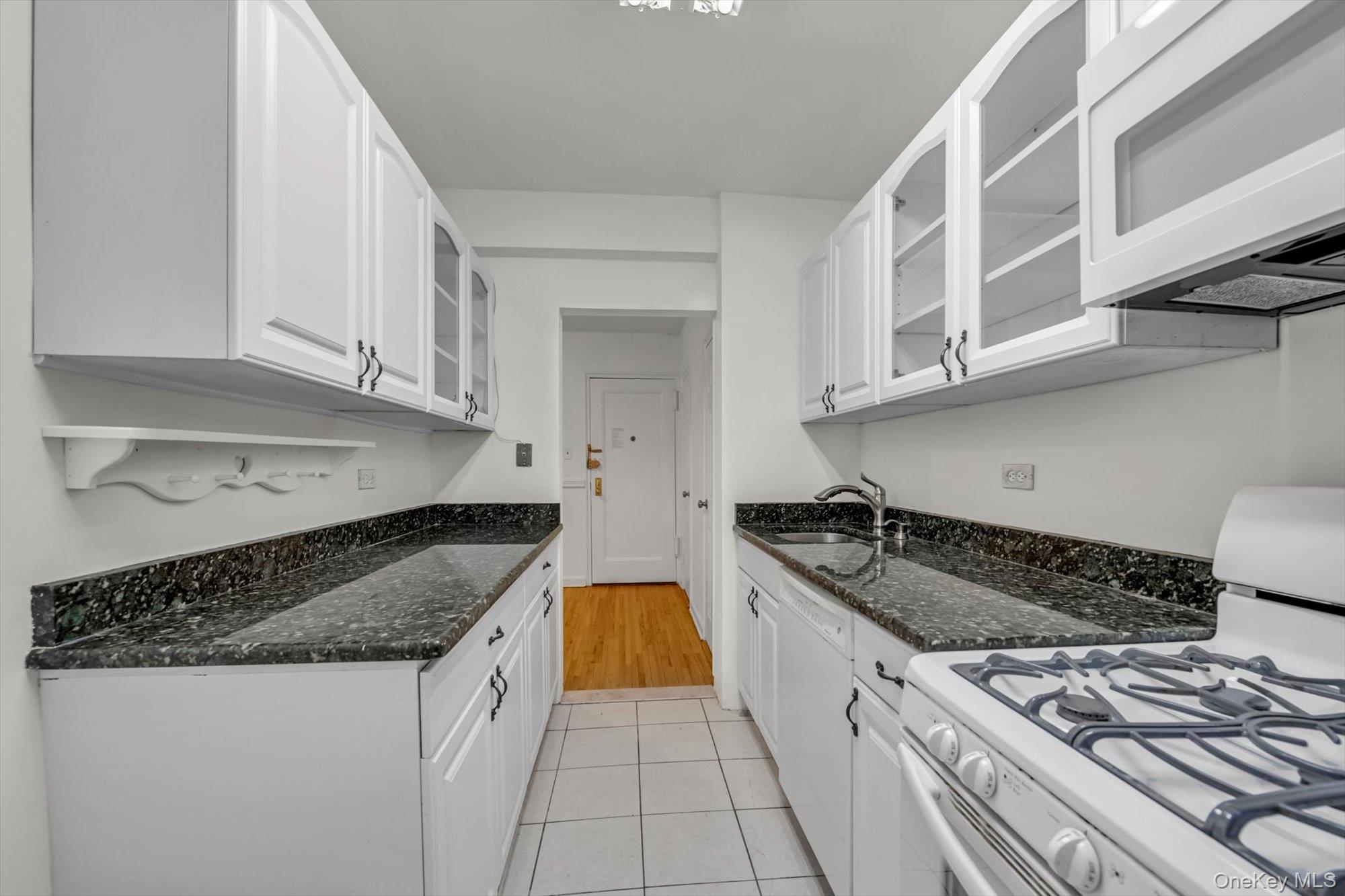 123-35 82nd Road, Unit 4H Queens, NY 11415 - Photo 6 of 15 Kitchen with white appliances, glass insert cabinets, white cabinetry, and dark stone countertops