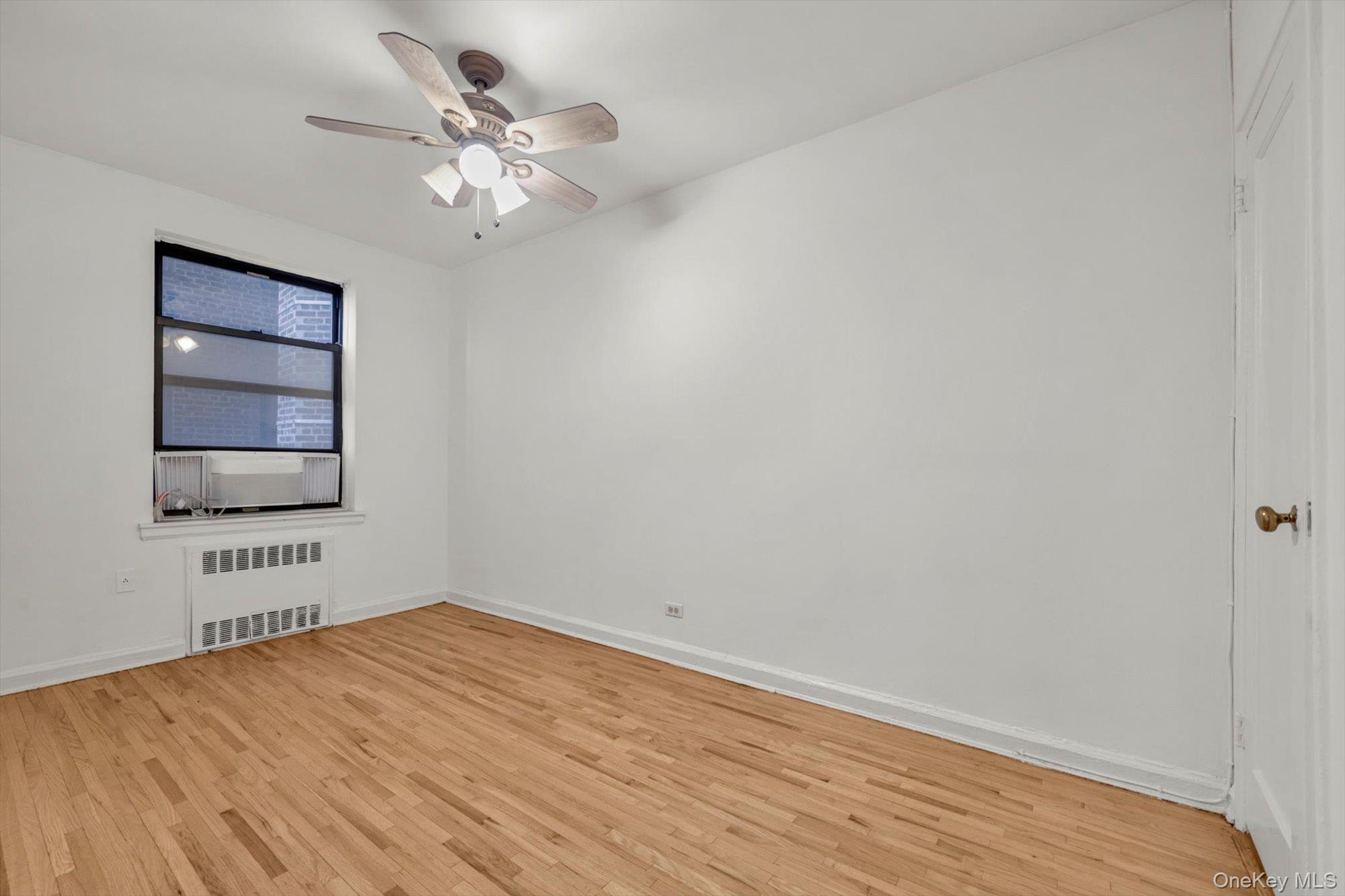 123-35 82nd Road, Unit 4H Queens, NY 11415 - Photo 9 of 15 Unfurnished room with radiator, light wood-style floors, and a ceiling fan