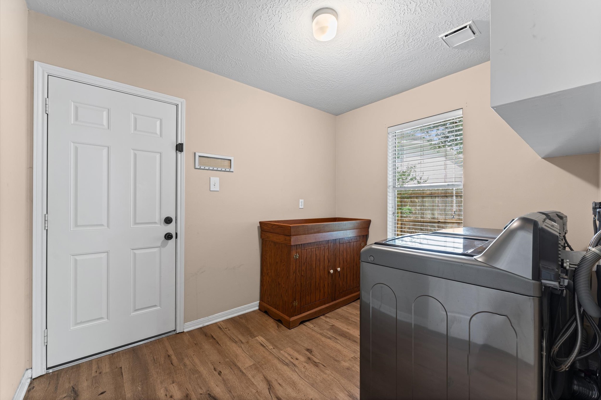 17618 Mill Springs Drive Spring, TX 77379 - Photo 15 of 26 This photo showcases a laundry room with a washer and dryer, laminate floor, a side cabinet, and a window allowing natural light. The neutral wall color and overhead lighting create a bright, functional space.