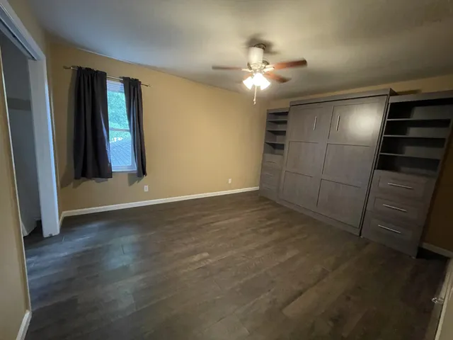 an empty room with wooden floor chandelier fan and windows