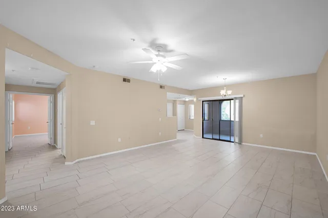 a view of an empty room with chandelier fan and window
