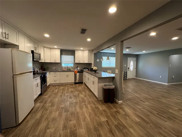 a large kitchen with stainless steel appliances granite countertop a refrigerator a sink dishwasher a stove and a microwave oven on the wooden floor