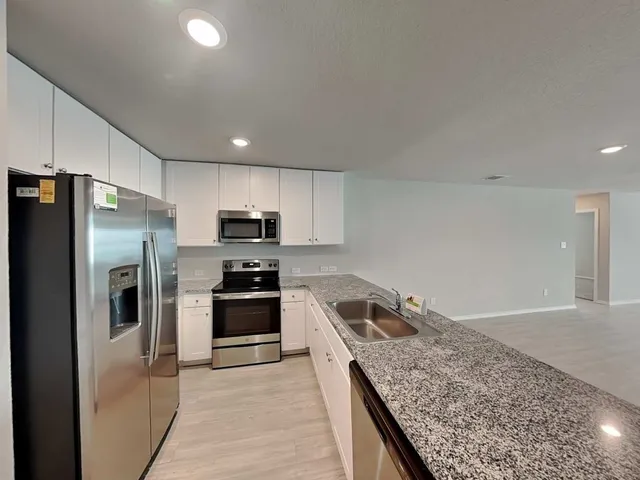 a view of a kitchen with kitchen island a sink wooden floor and stainless steel appliances