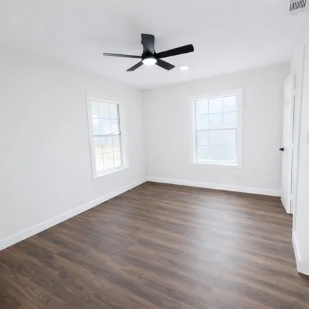 an empty room with wooden floor ceiling fan and windows