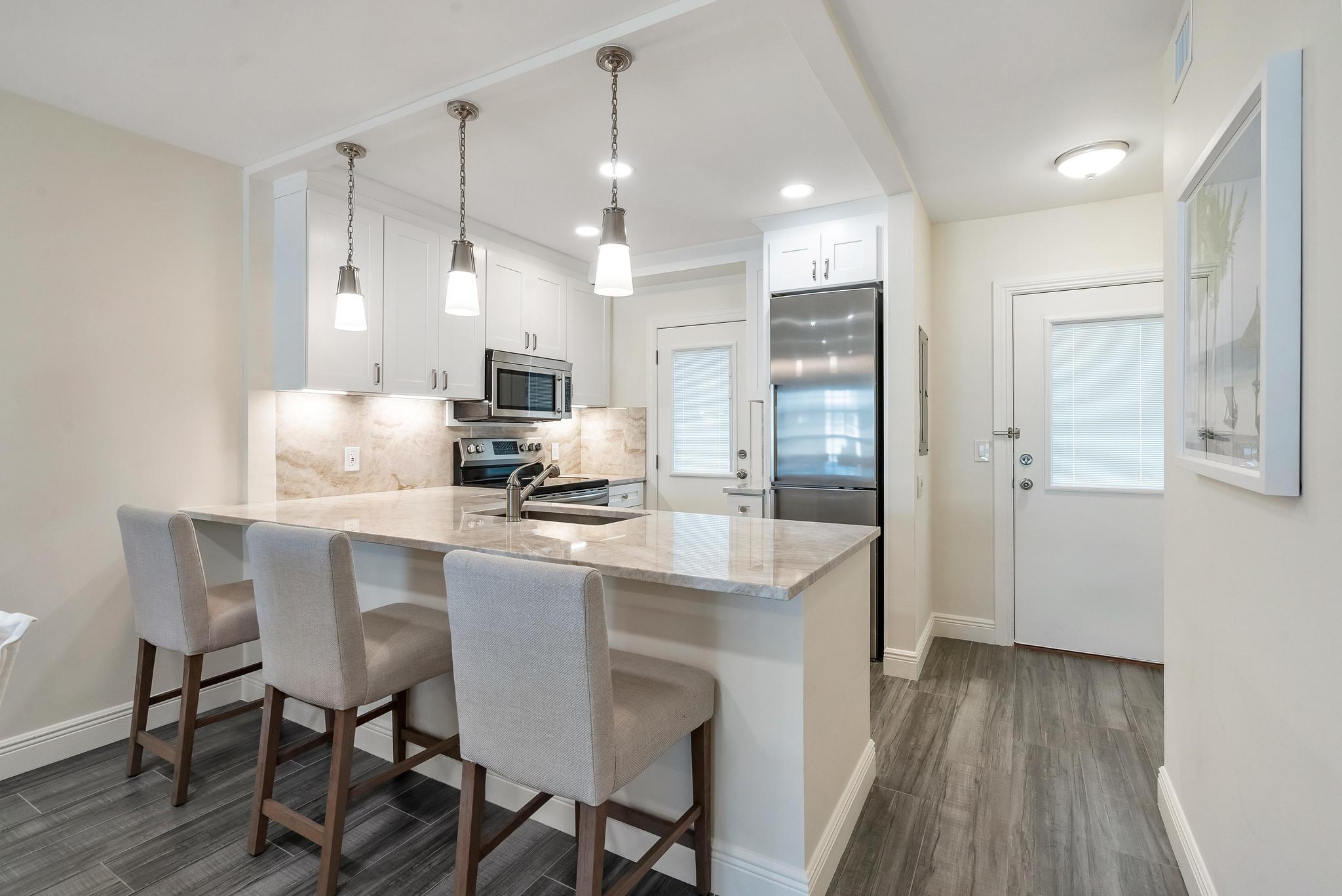 3851 North Ocean Boulevard, Unit 4100 Gulf Stream, FL 33483 - Photo 6 of 27 a kitchen with kitchen island granite countertop a table chairs refrigerator and microwave