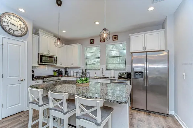 a kitchen with stainless steel appliances granite countertop a stove a refrigerator a sink a dining table and chairs with wooden floor