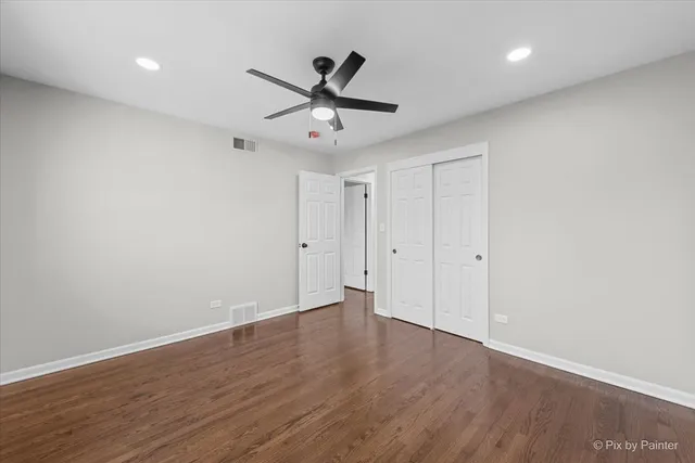 a view of an empty room with wooden floor and a ceiling fan