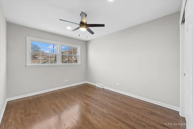 a view of an empty room with wooden floor and a ceiling fan