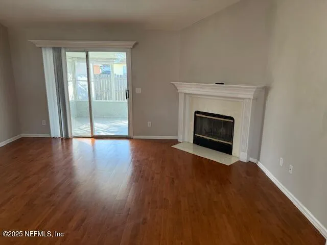 a view of an empty room with wooden floor fireplace and a window