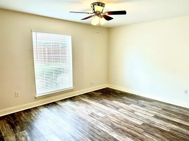 an empty room with wooden floor fan and windows