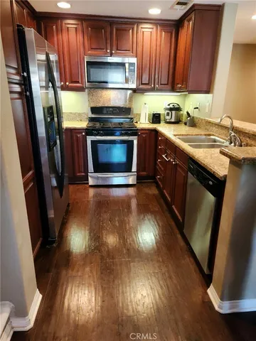 a kitchen with wooden floors wooden cabinets stainless steel appliances a sink and a window