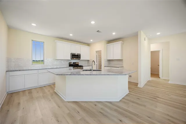 a large kitchen with stainless steel appliances granite countertop a stove a sink a refrigerator and white cabinets with wooden floor