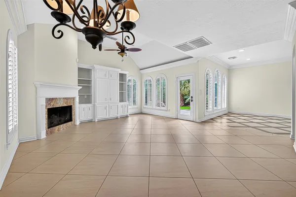 a view of an empty room with chandelier fan and kitchen view
