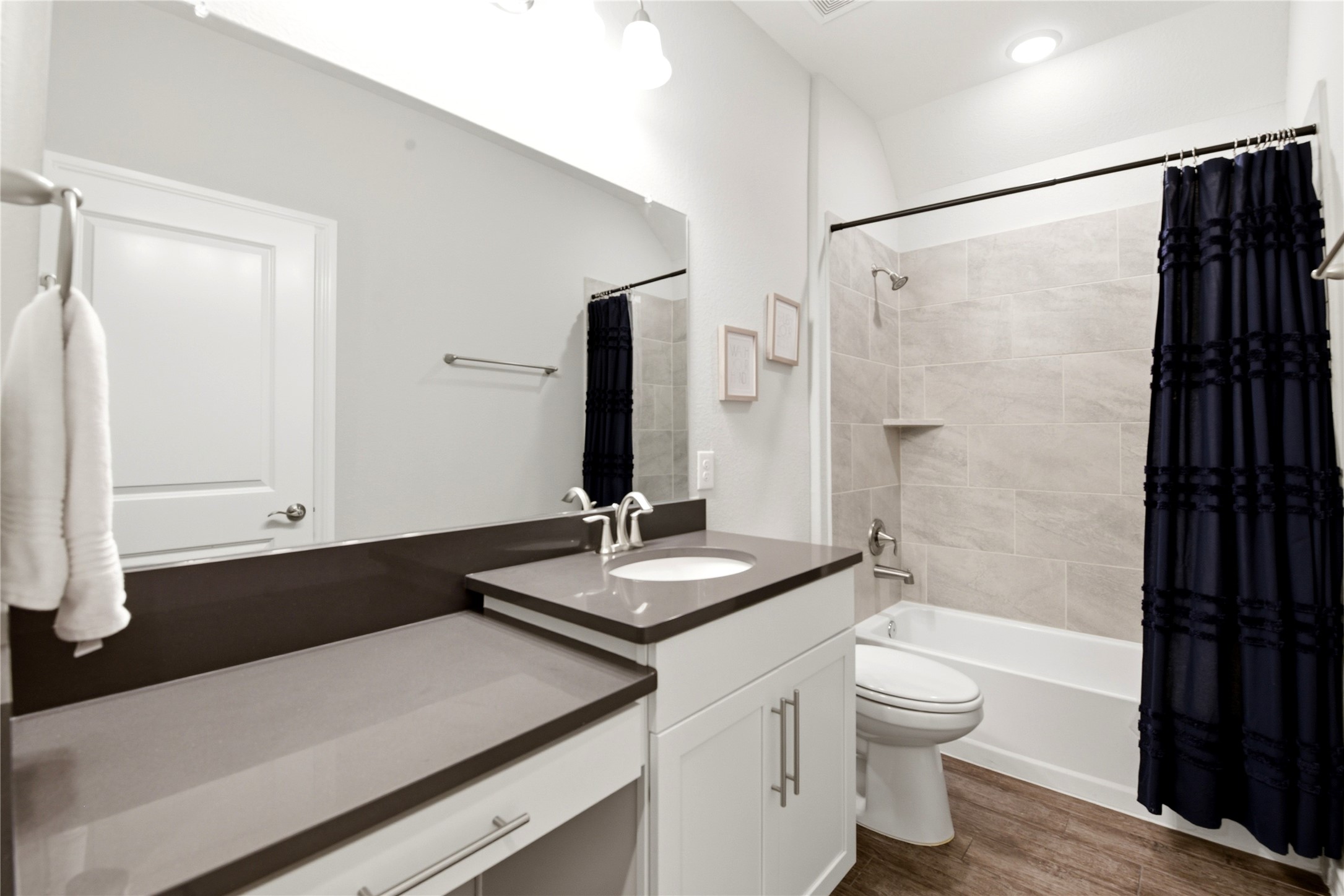 17834 Maple Ash Drive Spring, TX 77379 - Photo 30 of 50 Modern secondry bathroom with a sleek dark countertop, white cabinetry, and a large mirror. Features a bathtub with a tiled shower area. Warm
wood-like flooring complements the clean, bright aesthetic.
