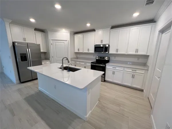 a kitchen with stainless steel appliances a stove top oven a refrigerator a sink and white cabinets