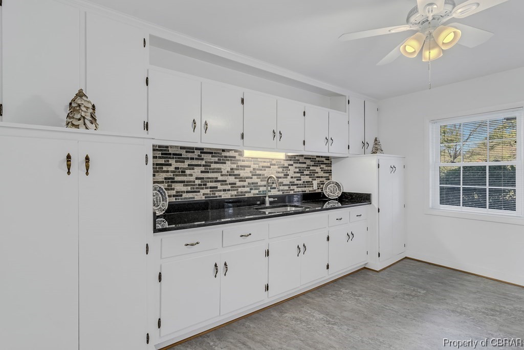 1057 Monaskon Road Lancaster, VA 22503 - Photo 20 of 43 Kitchen featuring sink, backsplash, dark stone counters, ceiling fan, and white cabinetry