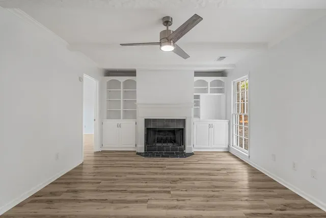 an empty room with wooden floor fireplace and windows