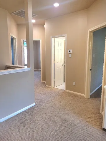 an empty room with chandelier fan and kitchen view