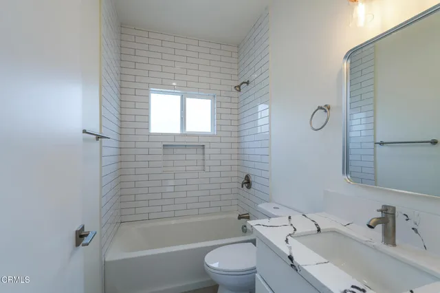 a bathroom with a bathtub shower sink vanity mirror and toilet