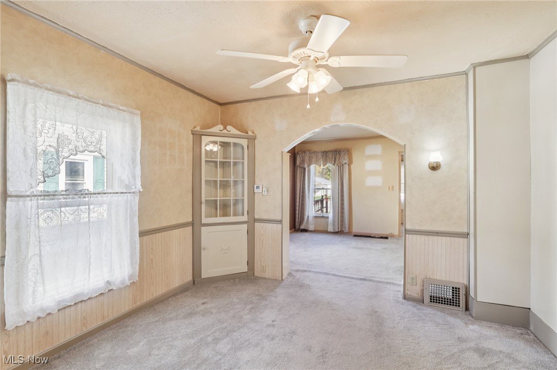 6235 Jefferson Road Ashtabula, OH 44004 - Photo 14 of 40 Empty room featuring a wainscoted wall, light colored carpet, arched walkways, wood walls, and a ceiling fan