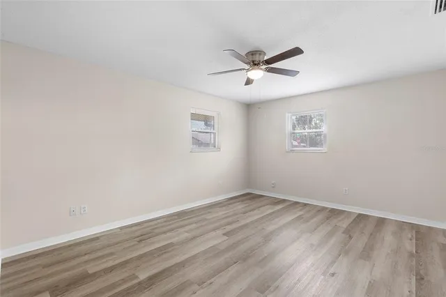 a view of an empty room with wooden floor and a ceiling fan