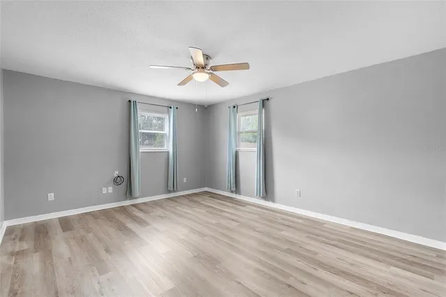 a view of an empty room with wooden floor and a ceiling fan