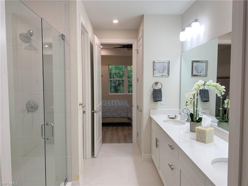 208 Indies Drive East, Unit 202 Naples, FL 34114 - Photo 19 of 48 a spacious en suite bathroom with a double vanity sink a large mirror a shower and vanity