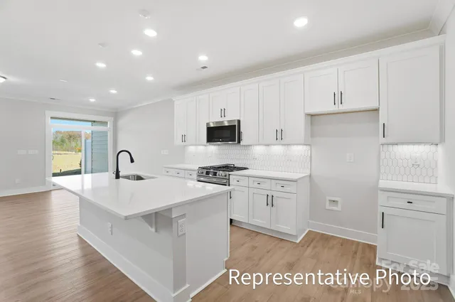 a large white kitchen with granite countertop a sink and dishwasher a stove with wooden floor