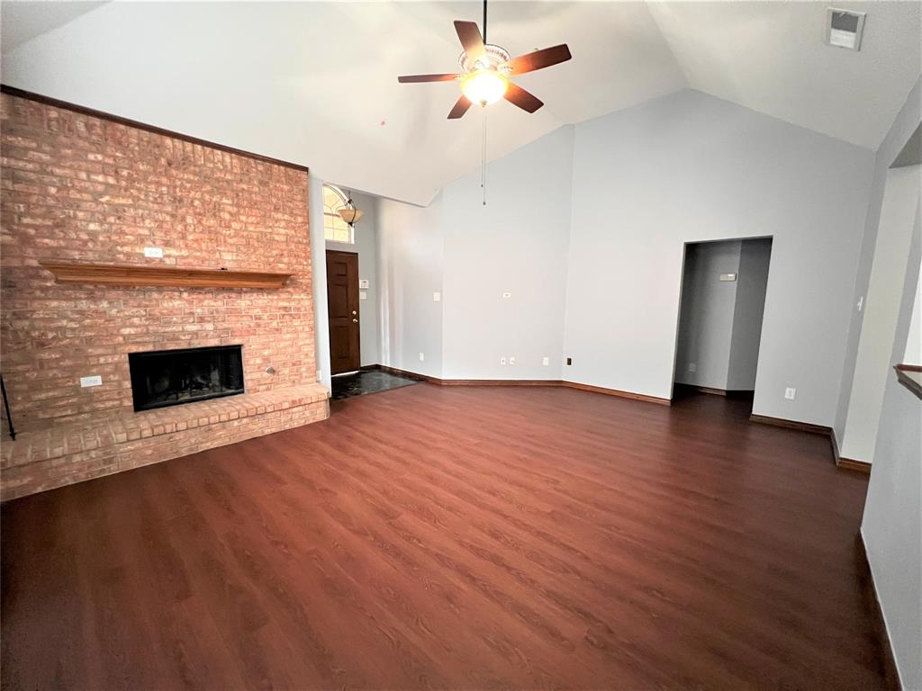 738 Ridgemont Drive Allen, TX 75002 - Photo 11 of 21 Spacious living area featuring a vaulted ceiling, wood-finish flooring, and a brick fireplace with a wood mantel