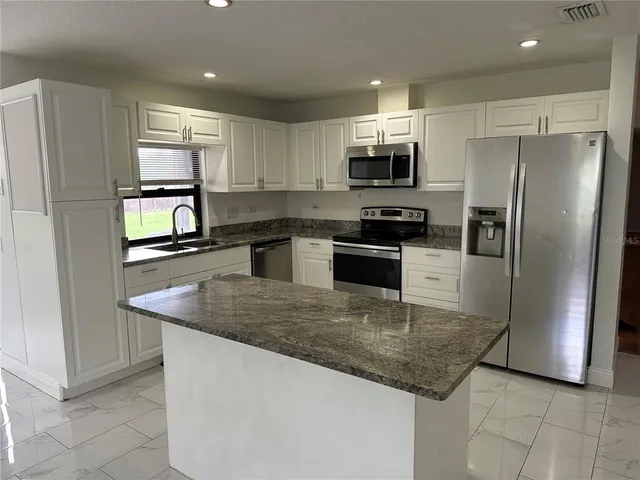 a kitchen with stainless steel appliances granite countertop a refrigerator a sink a stove a microwave and island