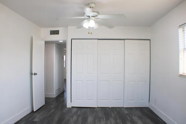 an empty room with wooden floor fan and windows