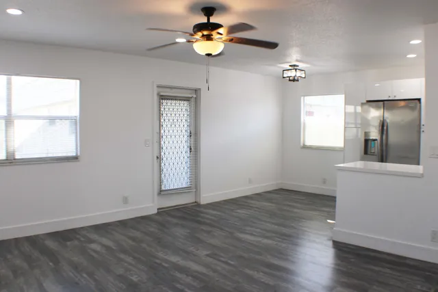 an empty room with wooden floor chandelier fan and windows