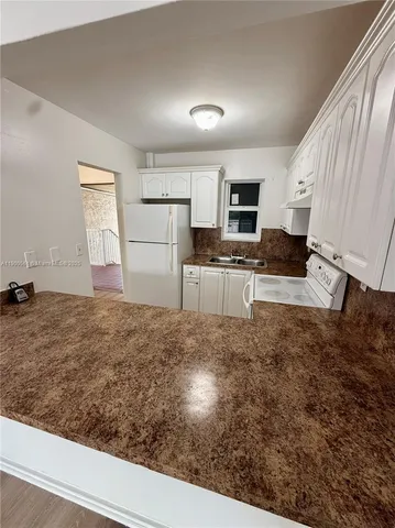 a view of kitchen and empty room with wooden floor