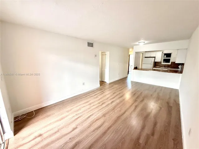 a view of a kitchen with kitchen island a sink wooden floor and an empty room