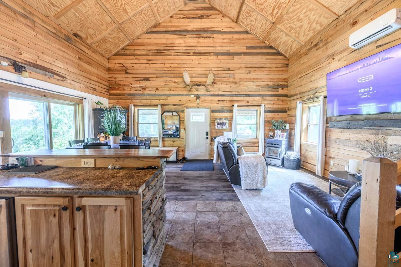7603 Levander Road Embarrass, MN 55732 - Photo 8 of 51 Vaulted wood-paneled ceiling, wood-plank walls, stone-wrapped kitchen island with wood cabinetry, large sliding glass doors, and tiled flooring
