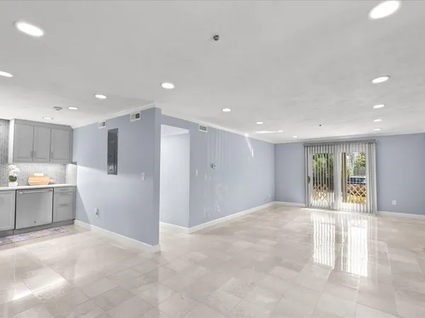 a view of an empty room with kitchen and window