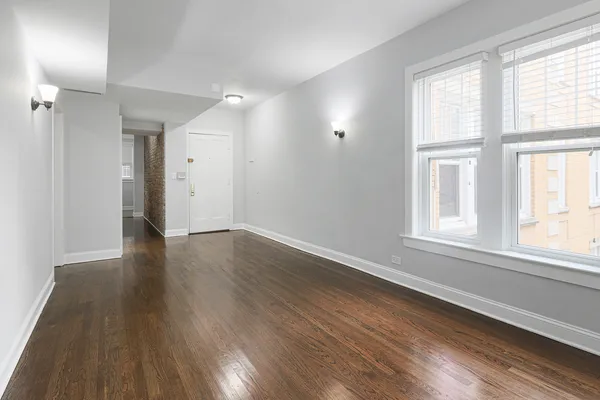 a view of an empty room with wooden floor and a window