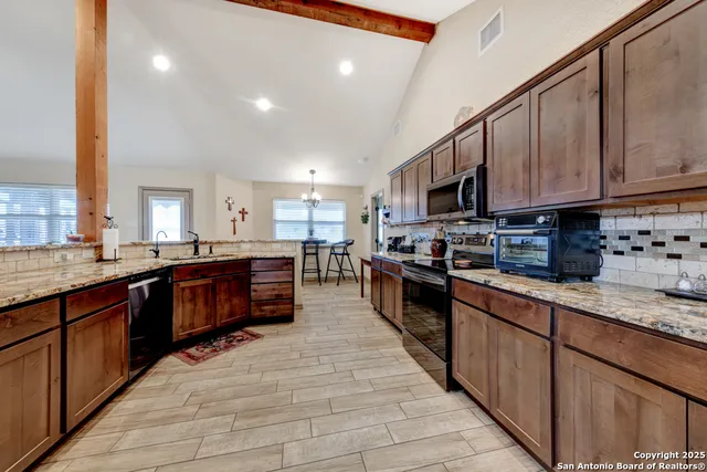 a large kitchen with stainless steel appliances granite countertop a large counter top a stove a sink a oven with wooden cabinets