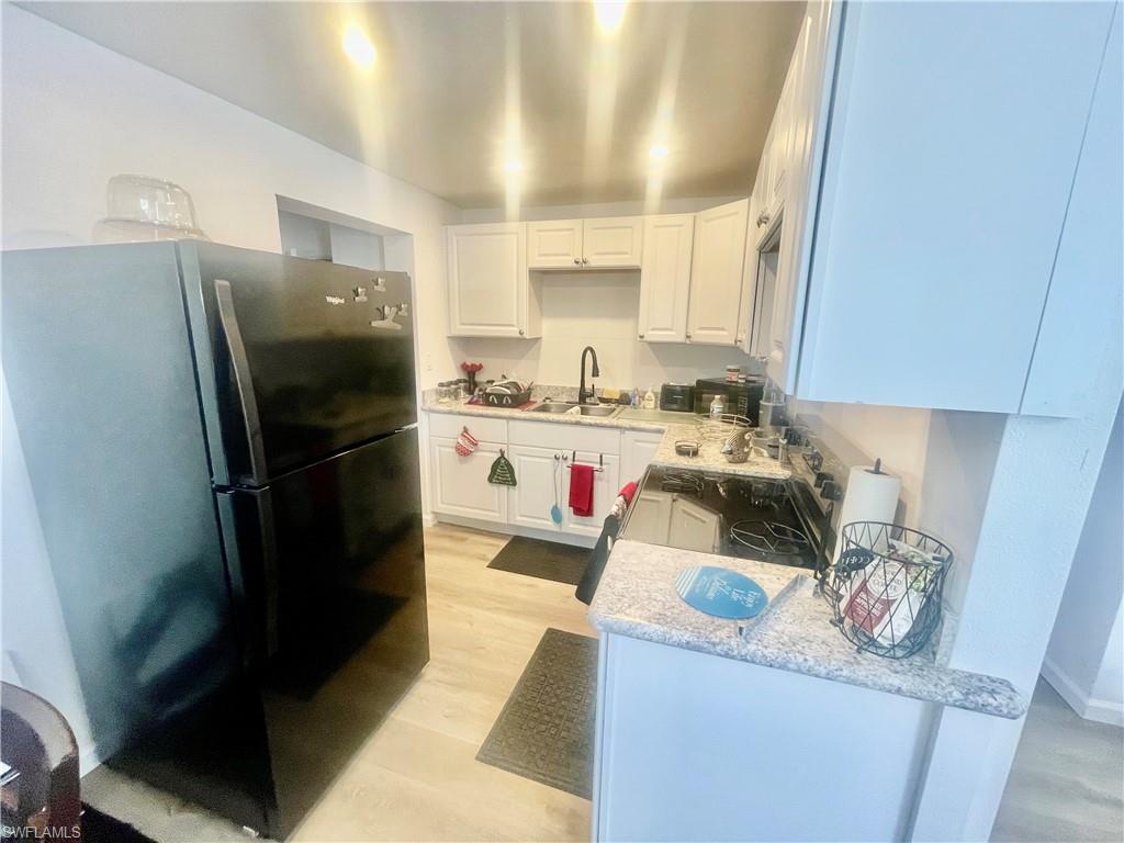 1339 5th Avenue North Naples, FL 34102 - Photo 5 of 17 Kitchen with freestanding refrigerator, white cabinetry, light stone counters, and light wood-style flooring