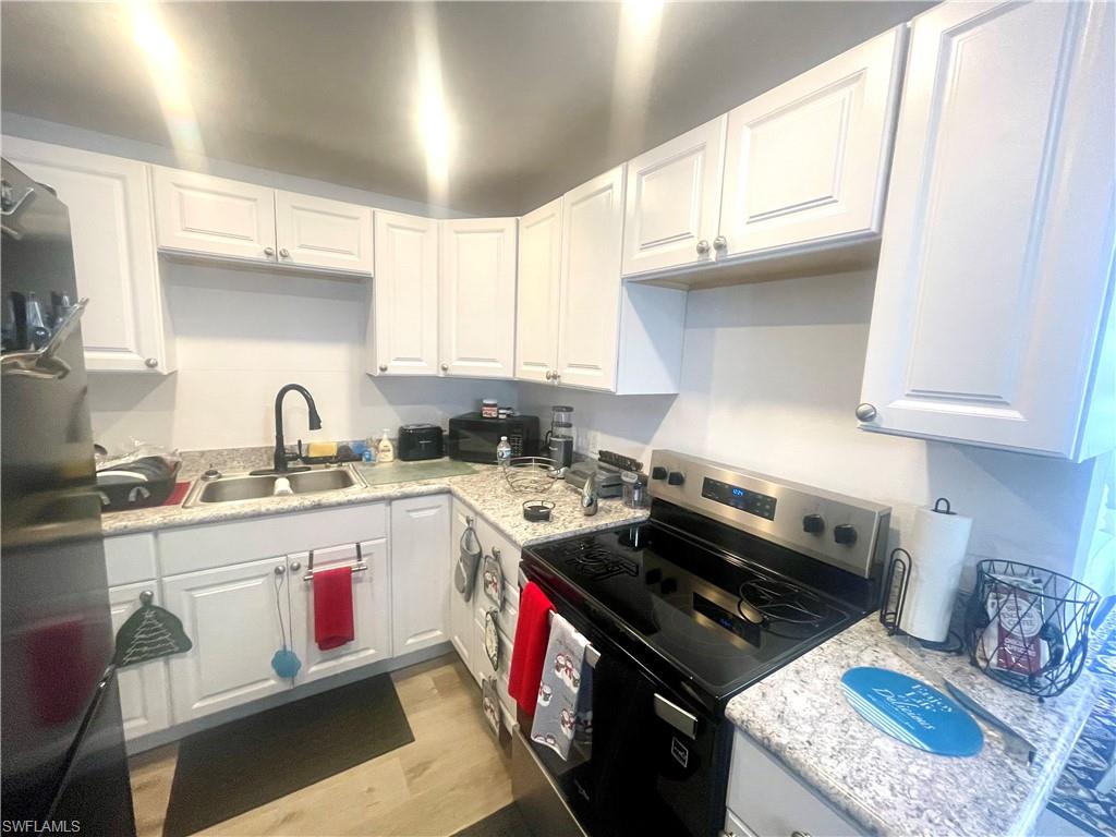 1339 5th Avenue North Naples, FL 34102 - Photo 6 of 17 Kitchen with stainless steel electric stove, white cabinets, fridge, light wood-type flooring, and black microwave