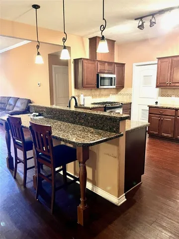 a kitchen with stainless steel appliances granite countertop a stove top oven a sink a dining table and chairs with wooden floor