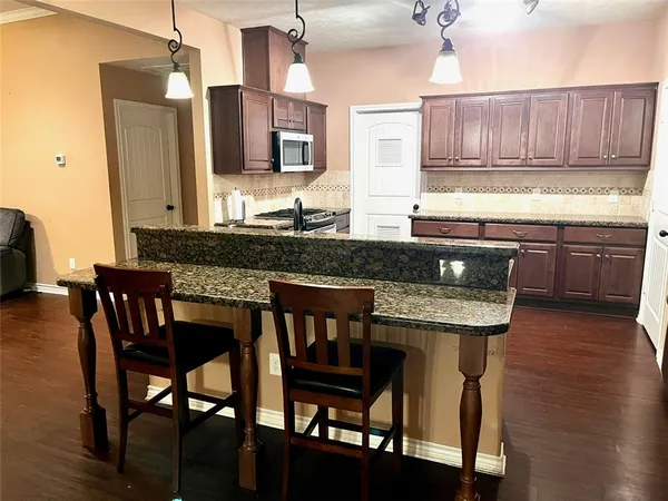 a kitchen with granite countertop a table chairs stove microwave and cabinets