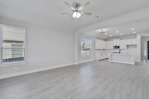 a view of an empty room with kitchen and window