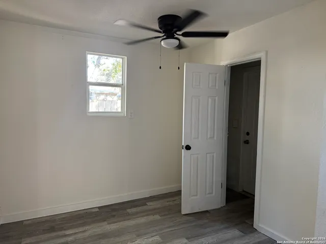 a view of an empty room with wooden floor and a ceiling fan