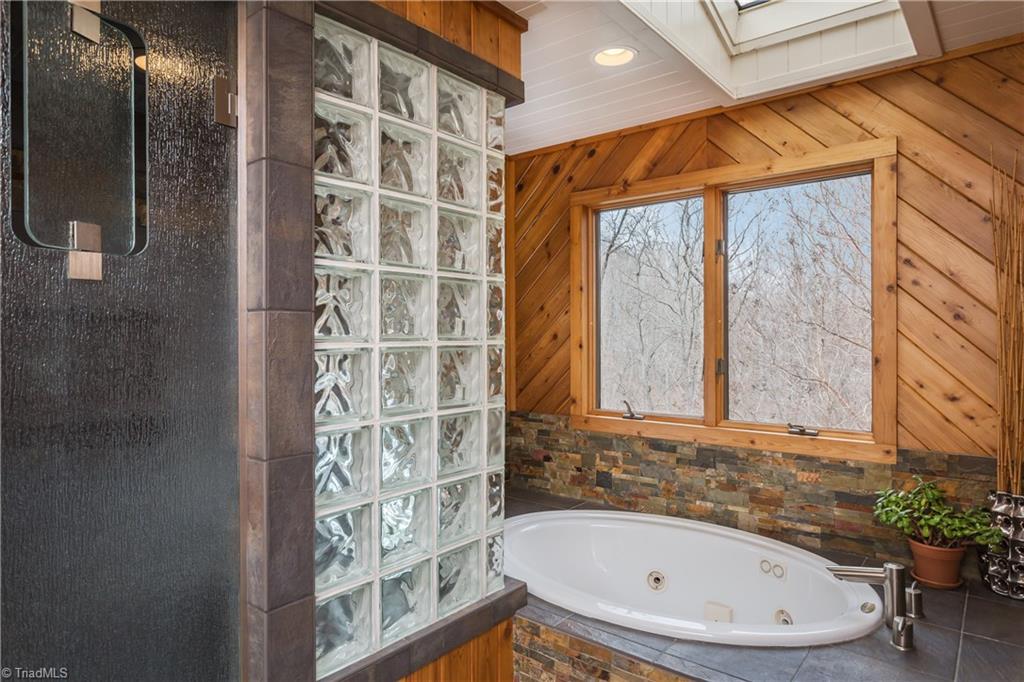 6111 Meadow Bluff Lane Oak Ridge, NC 27310 - Photo 21 of 30 The master shower has dual vanities, a jetted tub, glass encased steam shower with a dcor of wood and stone. Skylights provide additional light with recessed and sconce lighting. Large his and hers separate closets.