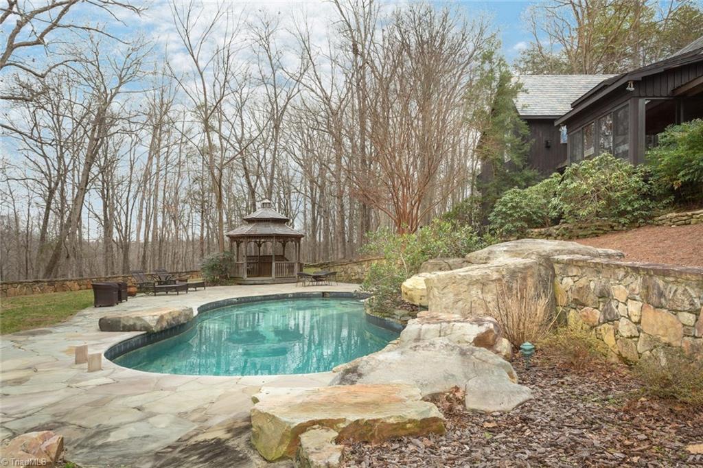 6111 Meadow Bluff Lane Oak Ridge, NC 27310 - Photo 4 of 30 Rock waterfall cascades into the salt water free form pool surrounded by stone walls and expansive flagstone patio. Gazebo and firepit on one side and the 1200 SF guest house on the other.